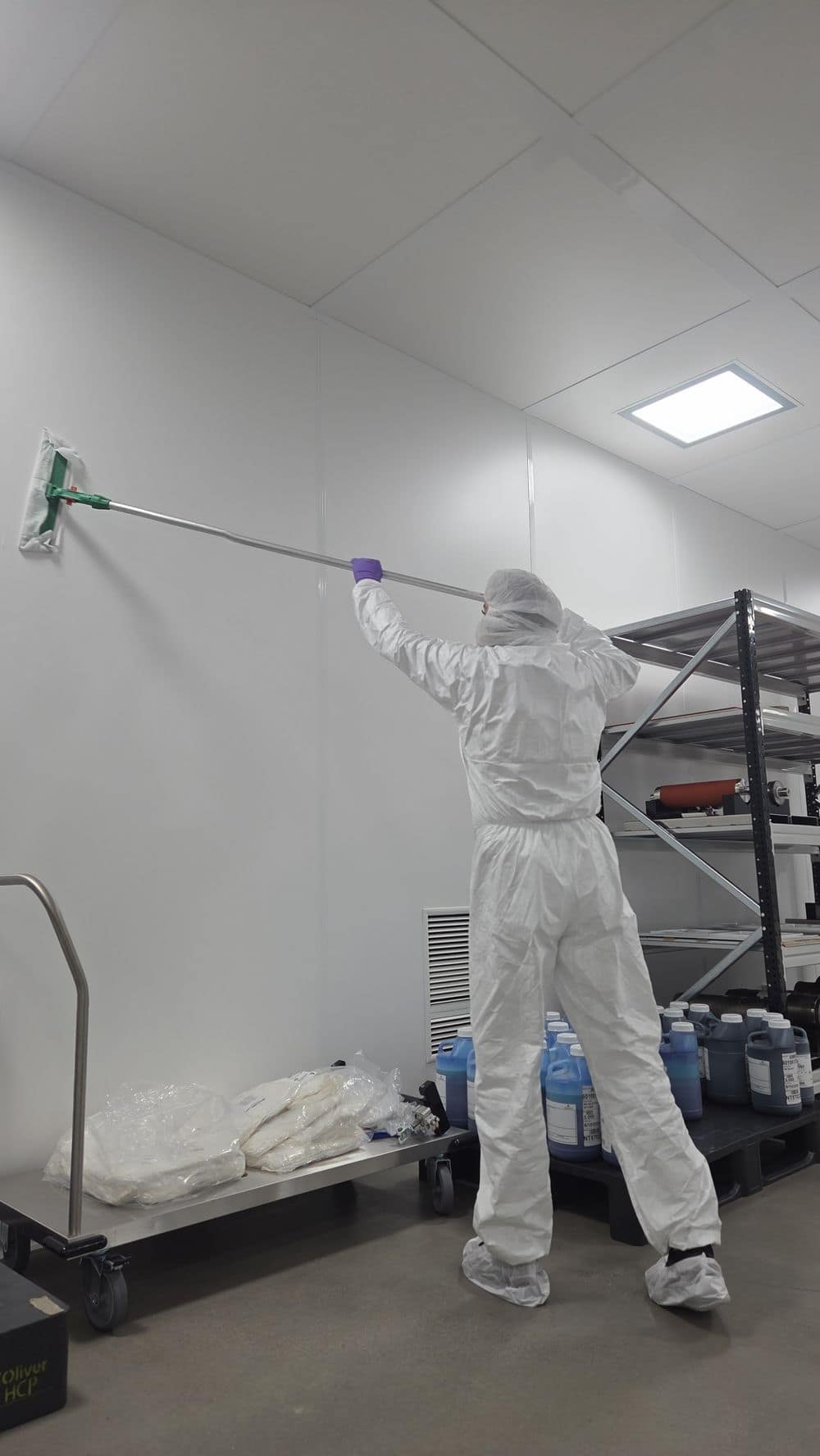 Medewerker van BrosCS in cleanroompak reinigt een wand met een vlakmop.